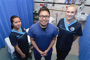 A male doctor and two female nurses stand in an emergency department treatment bay