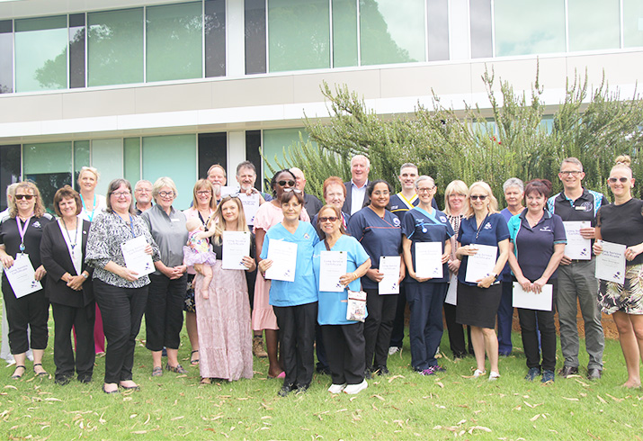 A group of Rockingham Peel Group staff stand outside the hospital holding long service leave certificates.