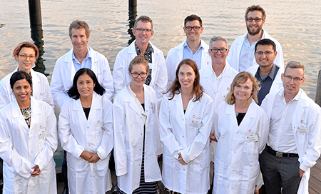 A group of male and female researchers wearing white lab coats standing outside