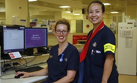 Two female nurses wearing Fremantle Hospital uniforms stand next to two computer screens.
