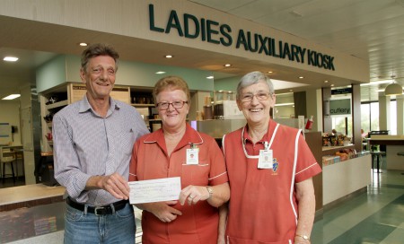 A man presenting a cheque to two women under a sign for the Ladies Auxiliary Kiosk