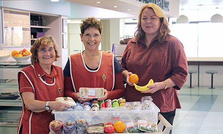 Three women stand behind a trolley that holds healthy fruit and drink options.