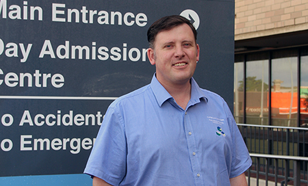 John Harris stands in front of a sign that reads 'Main entrance' and Day Admission Centre'.