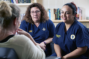 Two female nurses sitting down in conversation with another woman